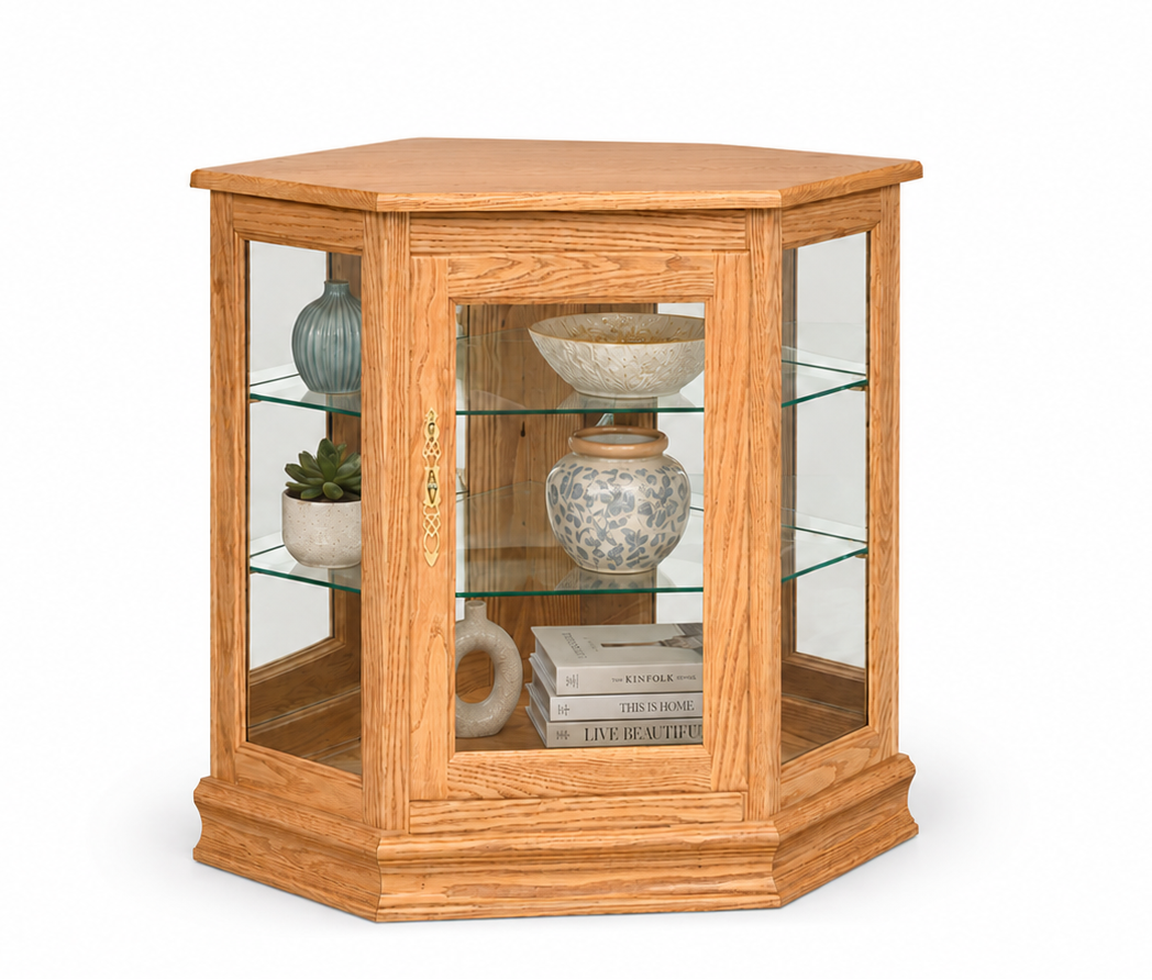 A hexagonal wooden display cabinet with glass doors and three glass shelves, shown on a plain white background. The cabinet is filled with decorative ceramic vases, a bowl, and books.
