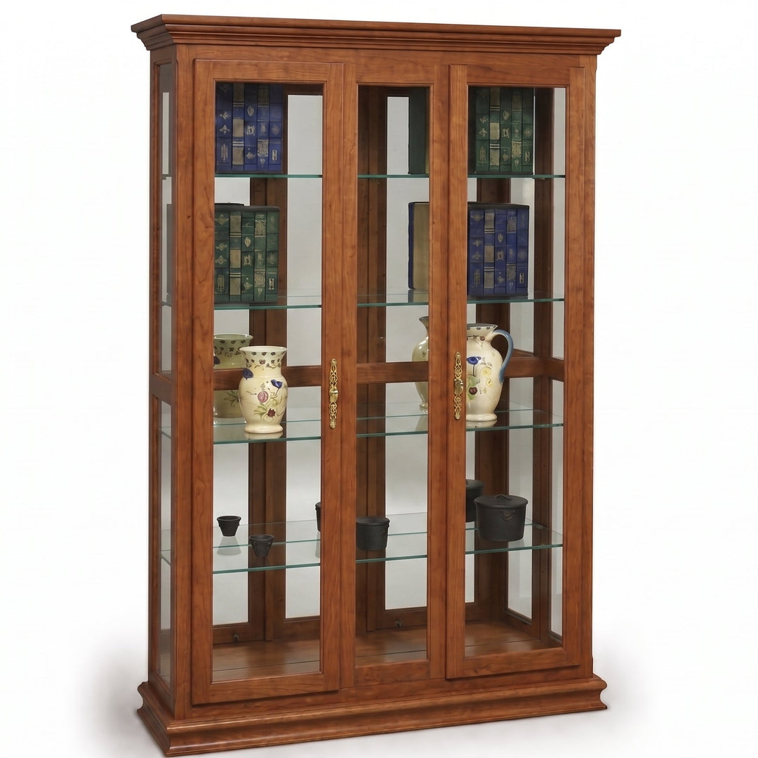 A tall wooden display cabinet with glass doors and multiple glass shelves, shown against a plain white background. The cabinet is made of warm medium-brown wood and contains decorative books and ceramic pitchers.