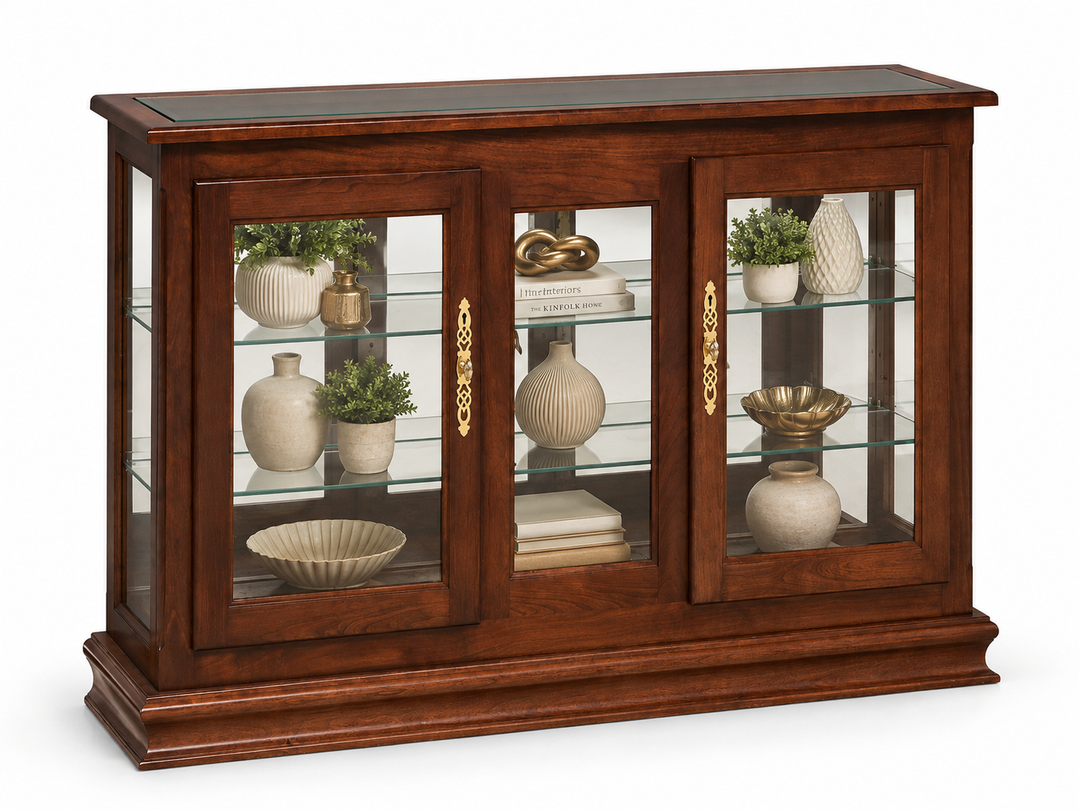 A dark brown wooden display cabinet with three glass-paneled doors and gold handles, showcasing glass shelves filled with decorative vases, bowls, and small potted plants, set against a plain white background.