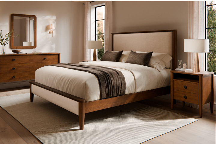 A Bryce Collection bedroom set including a bed with a beige headboard, a dresser, a mirror, and a nightstand, all in a brown maple finish.